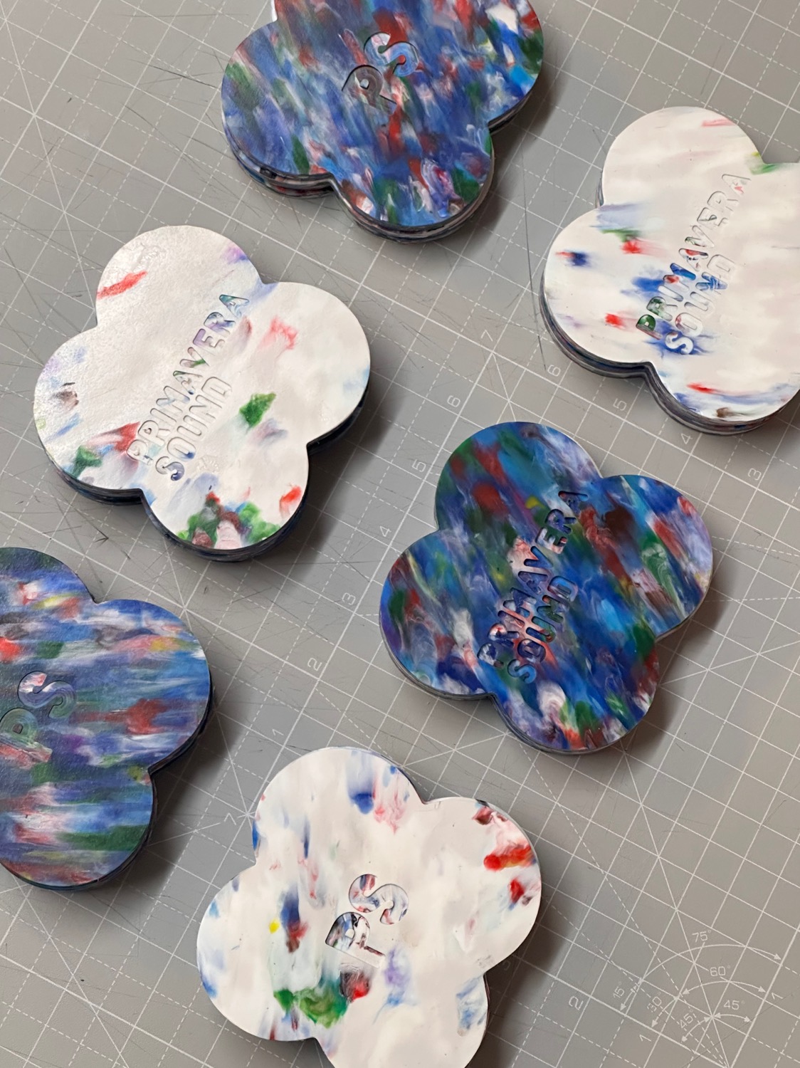 Flower-shaped recycled-plastic coasters mottled in blue, red and white, each embossed with a brand name