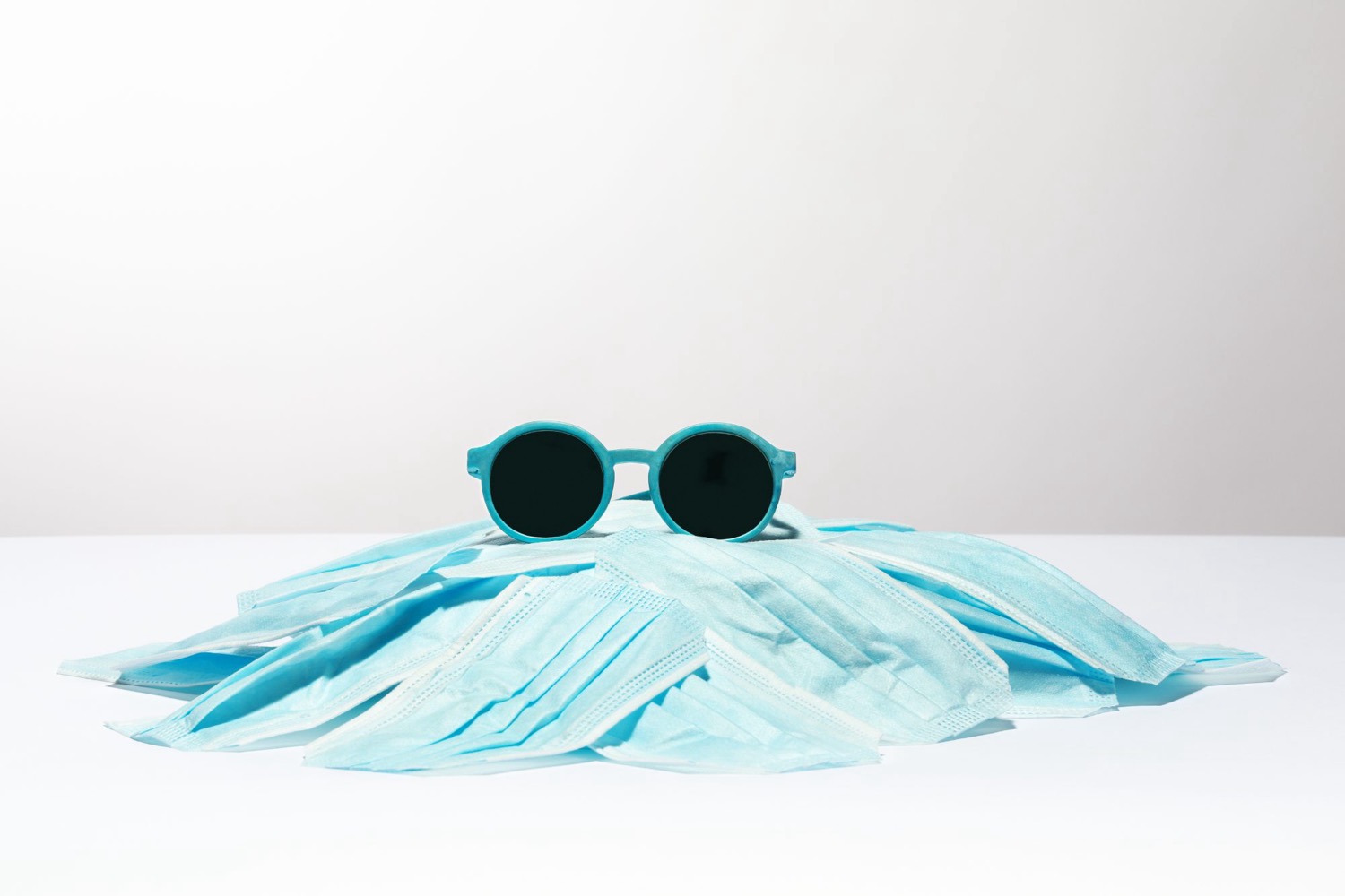 Sunglasses with dark round lenses resting on a mound of discarded blue face masks